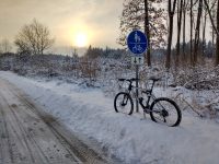Fahrrad an einen Schildpfosten gelehnt, die Sonne geht auf. Schnee überall