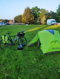 ein große wiese eines campingplatz, fast leer, ein fahrrad und ein zelt im vordergrund